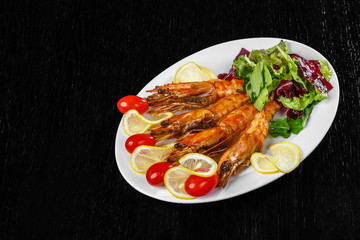 Shrimps, tomatoes and lemon are beautifully laid out on a dish on a black background.