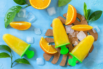 Homemade popsicles with orange juice, fruit ice, lollipops on a blue stone or slate background. Top...