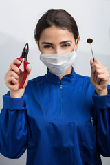 Dentista donna con mascherina chirurgica e camice blu mostra gli strumenti di lavoro in un amano e...
