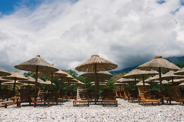 Sunbeds and umbrellas on a deserted pebble beach in cloudy weather on a background of clouds in Budva, Montenegro.