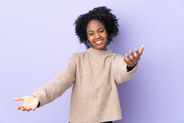 Young African American woman isolated on purple background presenting and inviting to come with hand