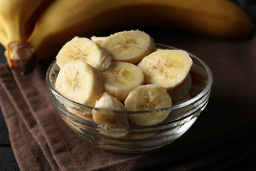Bowl of banana slices, banana and towel on wooden background