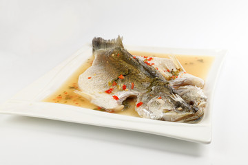Thai style steam sea bass barramundi with lemon garlic chilli clear sauce on white serving dish