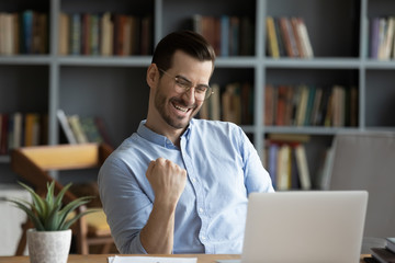 Excited man wearing glasses celebrating success, reading good news in email, happy overjoyed...