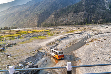 A Nepalese driver washes his bus driving straight into a mountain river, amid a valley and mountains.