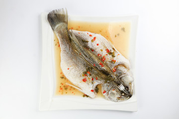 Thai style steam sea bass barramundi with lemon garlic chilli clear sauce on white serving dish