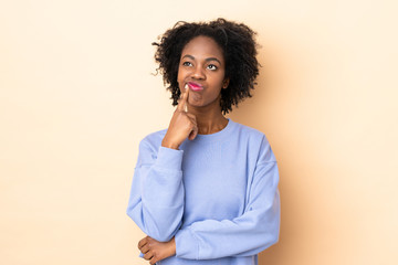 Fototapeta na wymiar Young African American woman isolated on beige background having doubts while looking up