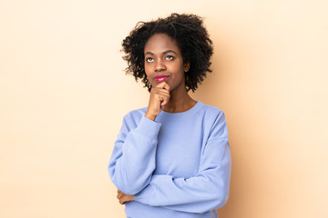 Young African American woman isolated on beige background and looking up