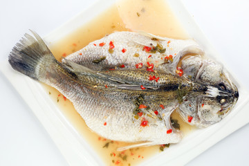 Thai style steam sea bass barramundi with lemon garlic chilli clear sauce on white serving dish