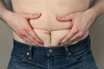 Fototapeta premium Man in jeans hold his fat belly. Weight gain