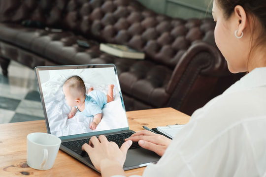 safety, technology and family concept - mother watching her baby on bed by video monitor on laptop from home to prevent corona virus