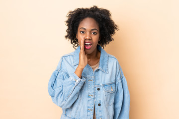 Fototapeta na wymiar Young African American woman isolated on beige background whispering something with surprise gesture while looking to the side