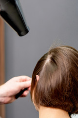 Fototapeta premium Close up of professional hairdresser is drying hair of woman, back view in hair salon.