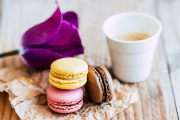 Trois macarons saveur citron framboise et chocolat posés sur du papier brun avec une tasse de...