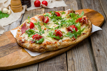 Pinsa with parma ham and aragula on wooden table, rome pizza.