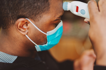 African american man using a temporal thermometer to record his temperature by running it across...