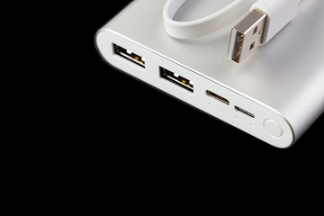 An additional stand-alone power bank for charging mobile devices. External battery isolated on a black background. White charger for smartphone, power supply (battery bank). Selective focus.