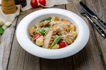 Salad caesar with chicken on white plate on wooden table