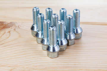 Automobile bolts. Metall bolts to fix the wheels of a car on a wood background in a photo studio. Spare consumables for replacing a wheel in a garage or workshop. Close-up.
