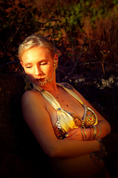 A Beautiful Young Woman Relaxes Between 
Large Quarry Rocks. She Is Covered In Gold 
Jewellery And Gold Glimmer.