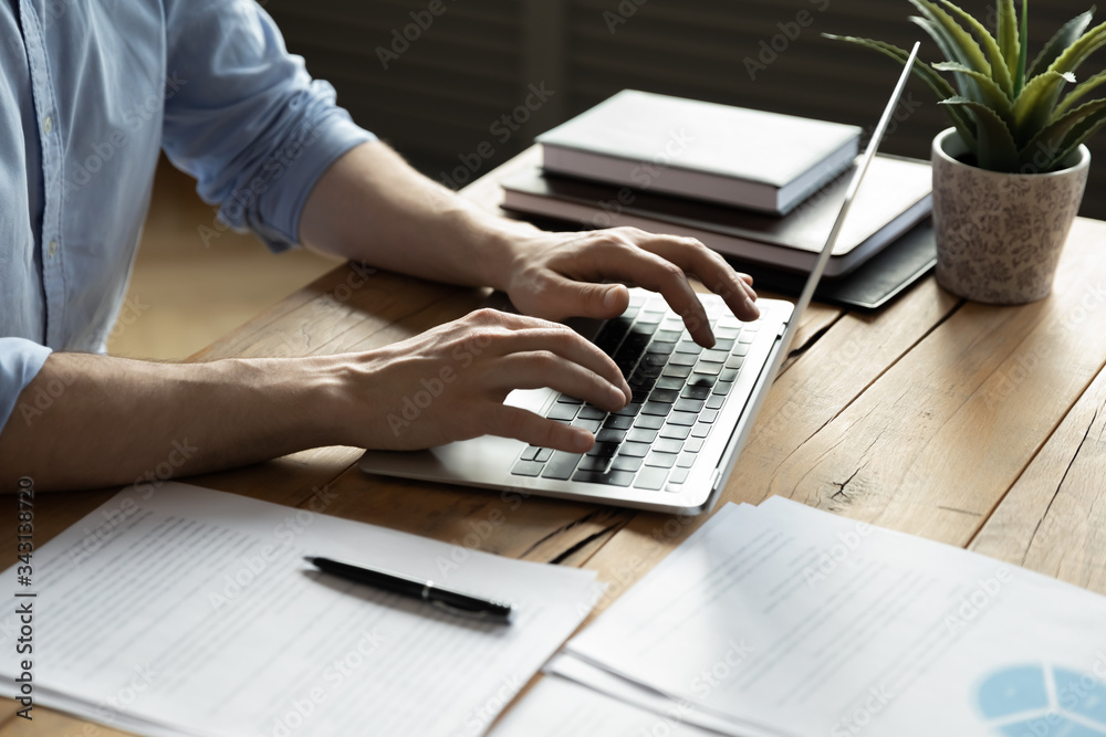 Wall mural close up businessman using laptop, typing on keyboard, sitting at wooden desk with documents, writin