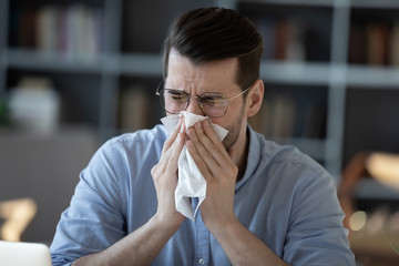 Close up unhealthy businessman blowing wiping running nose, using napkin, sick young man wearing...