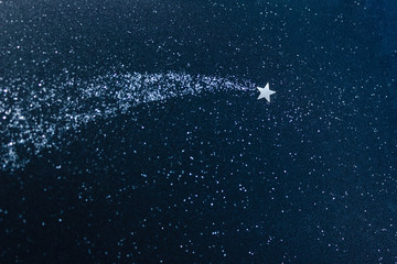 Silver confetti applique on a dark blue glitter of cardboard. Shooting star and stardust. The concept of a dream and make a wish. Selective focus. © ClareM