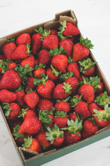 green paper box full of red strawberries on white wooden table background vertical