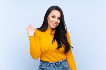 Young Colombian girl over isolated blue background saluting with hand with happy expression