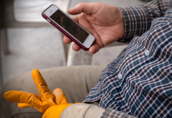 Worker wearing yellow gloves is looking on mobile during break