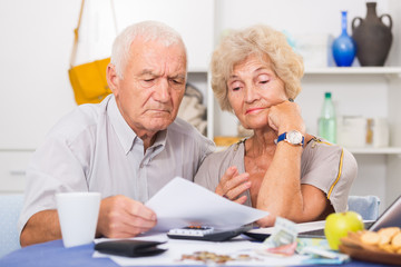 Worried mature man and woman analyzing bills