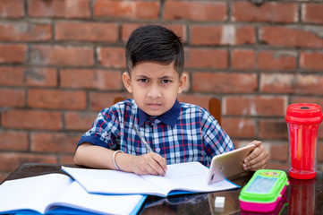 Smiling young male kid using digital smartphone watching online e-learning video to studying in classroom , Asian Indian schoolboy study with Mobile phone.