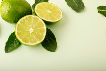 Fresh green limes on a pastel background. Mint leaves are laid out in the background and complement...