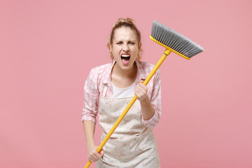 Crazy angry young woman housewife in casual clothes, apron doing housework isolated on pastel pink...