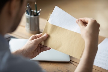 Close up businessman holding envelope with blank paper sheet, focused man looking at letter, received news, notification or invitation, working with correspondence, sitting at work desk - obrazy, fototapety, plakaty