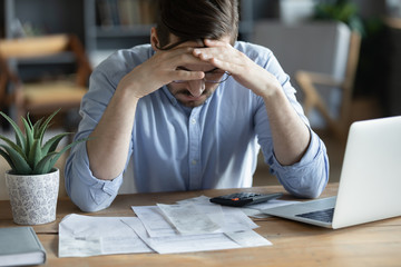 Sad depressed man checking bills, anxiety about debt or bankruptcy, financial problem, bank debt or lack of money, unhappy frustrated young male sitting at work desk with laptop and calculator - obrazy, fototapety, plakaty