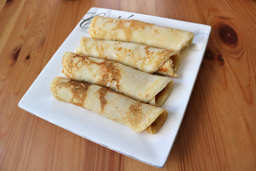 handmade crepes or pancakes baked recipe, in a square white plate on a wooden table - sweet rolled up, breakfast or dessert with tasty food