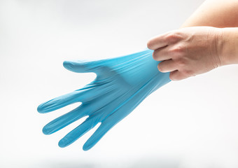 Woman pulls on her hand a blue latex medical glove on a white background. Horizontal orientation.