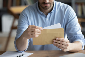 Focused businessman reading letter, looking at paper, holding envelope in hands close up, received news or important information, freelancer working with correspondence, sitting at work desk - obrazy, fototapety, plakaty