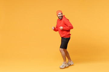 Fototapeta na wymiar Side view of cheerful young bearded fitness sporty guy sportsman in hat, hoodie, shorts spend weekend in home gym isolated on yellow background. Workout sport motivation lifestyle concept. Running.