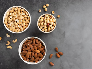 assorted nuts in white bowls on a gray concrete background. kernels almonds, hazelnuts, cashews. food background. place for text. top view.
