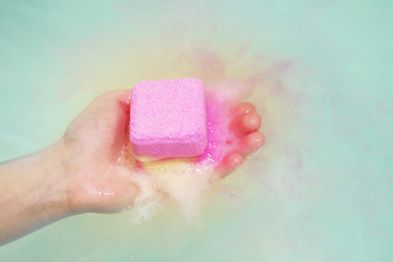 Cube of bath salt dissolves in water in female hand