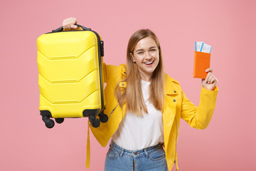 Funny young woman girl in yellow leather jacket posing isolated on pastel pink background studio portrait. People lifestyle concept. Mock up copy space. Hold suitcase passport tickets boarding pass.