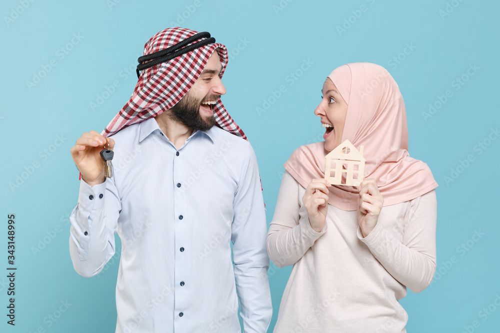 Wall mural Excited couple friends arabian muslim man wonam in keffiyeh kafiya ring igal agal hijab clothes isolated on blue background. People religious concept. Hold house bunch of keys, looking at each other.