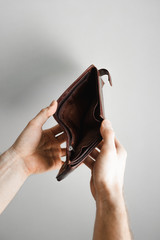Man's hands holding wallet with no money on the grey background