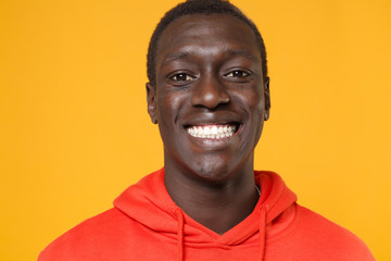 Close up of smiling young african american man guy in red streetwear hoodie posing isolated on yellow background studio portrait. People emotions lifestyle concept. Mock up copy space. Looking camera.
