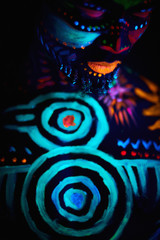 handsome young african guy with fluorescent prints on chest and other parts of body glowing in neon lights, uv rays. male fashion model posing, cosmic prints and body art concept