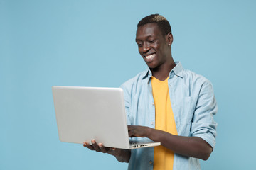 Smiling young african american man guy in casual shirt, yellow t-shirt posing isolated on blue background studio portrait. People lifestyle concept. Mock up copy space. Working on laptop pc computer.