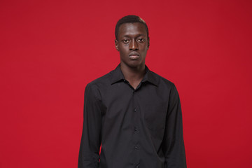 Obraz premium Serious young african american man guy in classic black shirt posing isolated on red wall background studio portrait. People sincere emotions lifestyle concept. Mock up copy space. Looking camera.