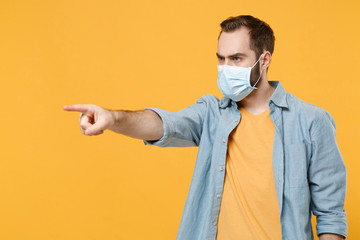 Displeased young man in sterile face mask posing isolated on yellow background. Epidemic pandemic...